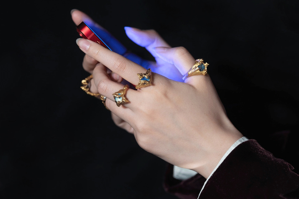 Detail of hands holding a phone wearing multiple gold rings set with large precious stones