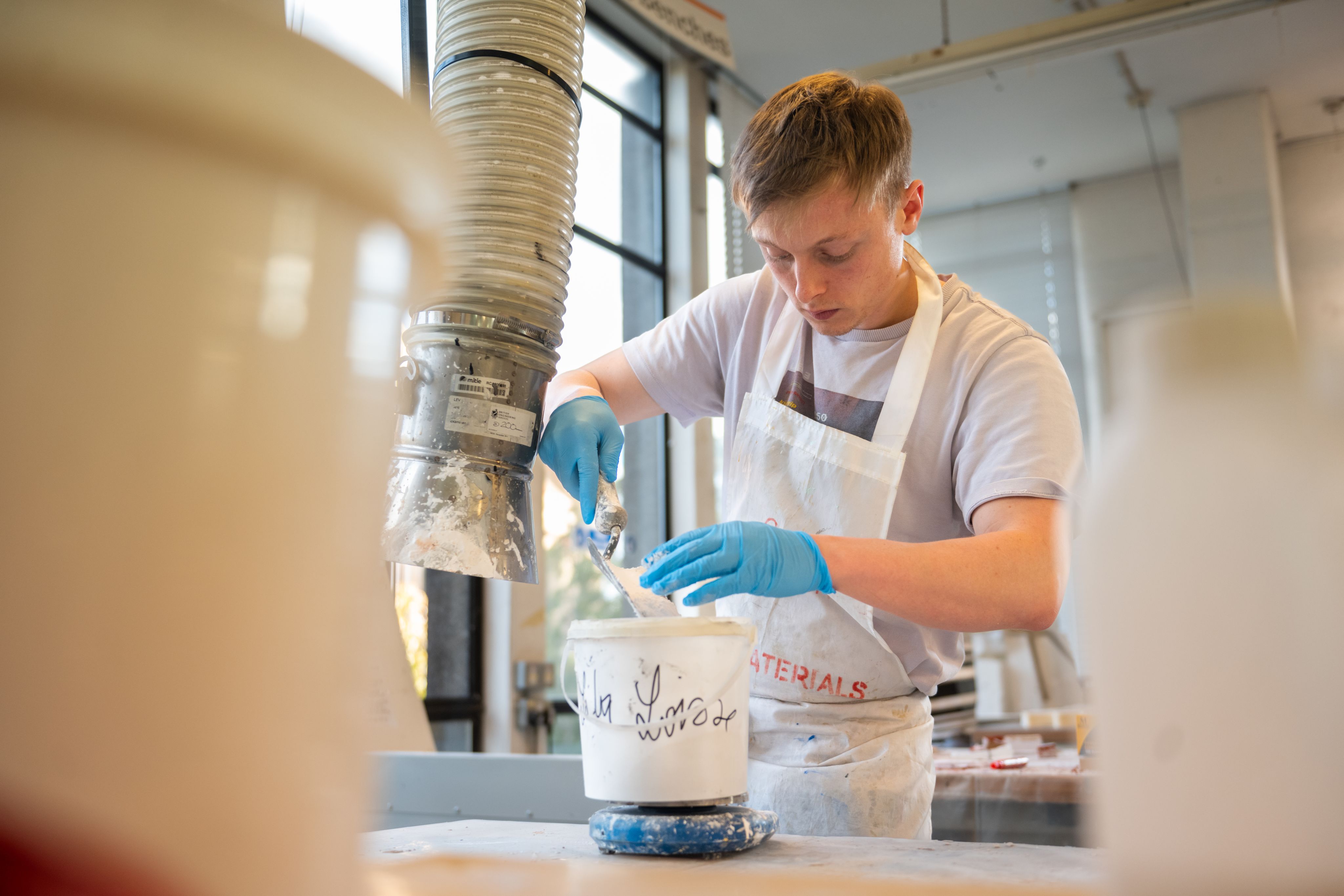 A student in a white apron mixing paint