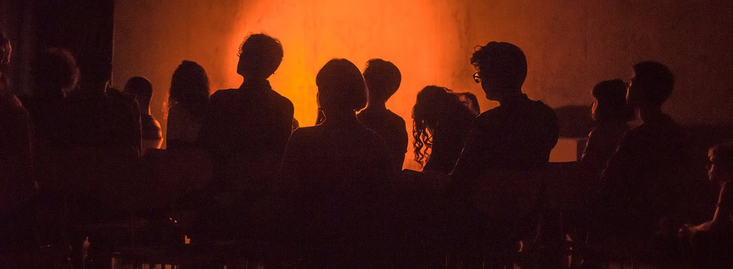 Silhouettes of exhibition visitors against a projection lit in orange 