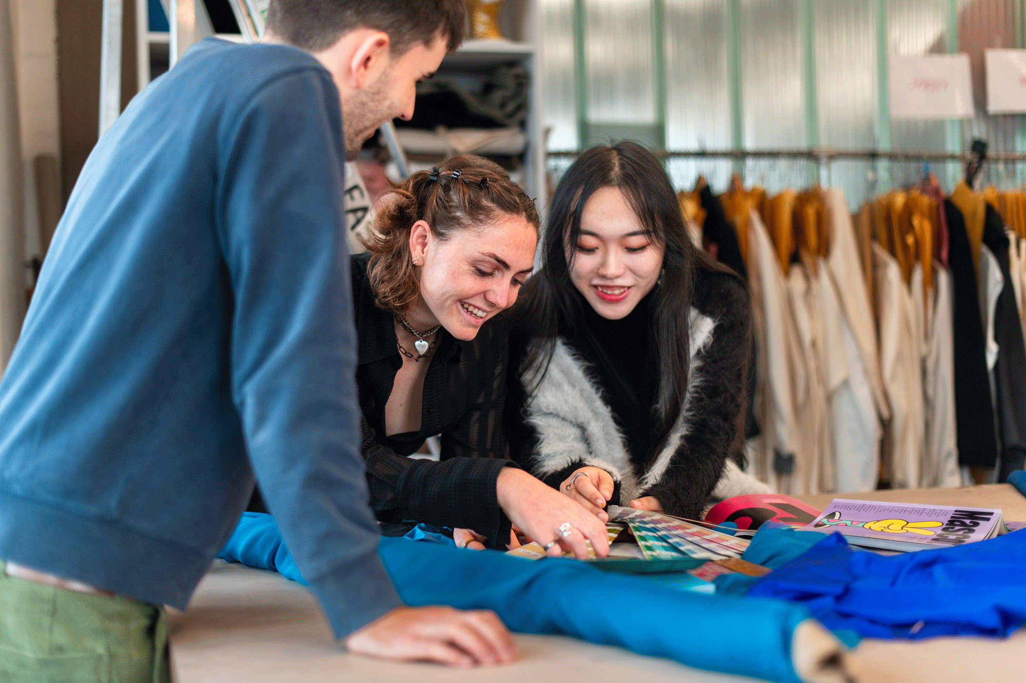 Three students n the fashion studios examine bolts of blue fabric against colour swatches