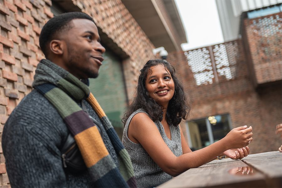 Two students seated at a table outdoors and engaged in conversation