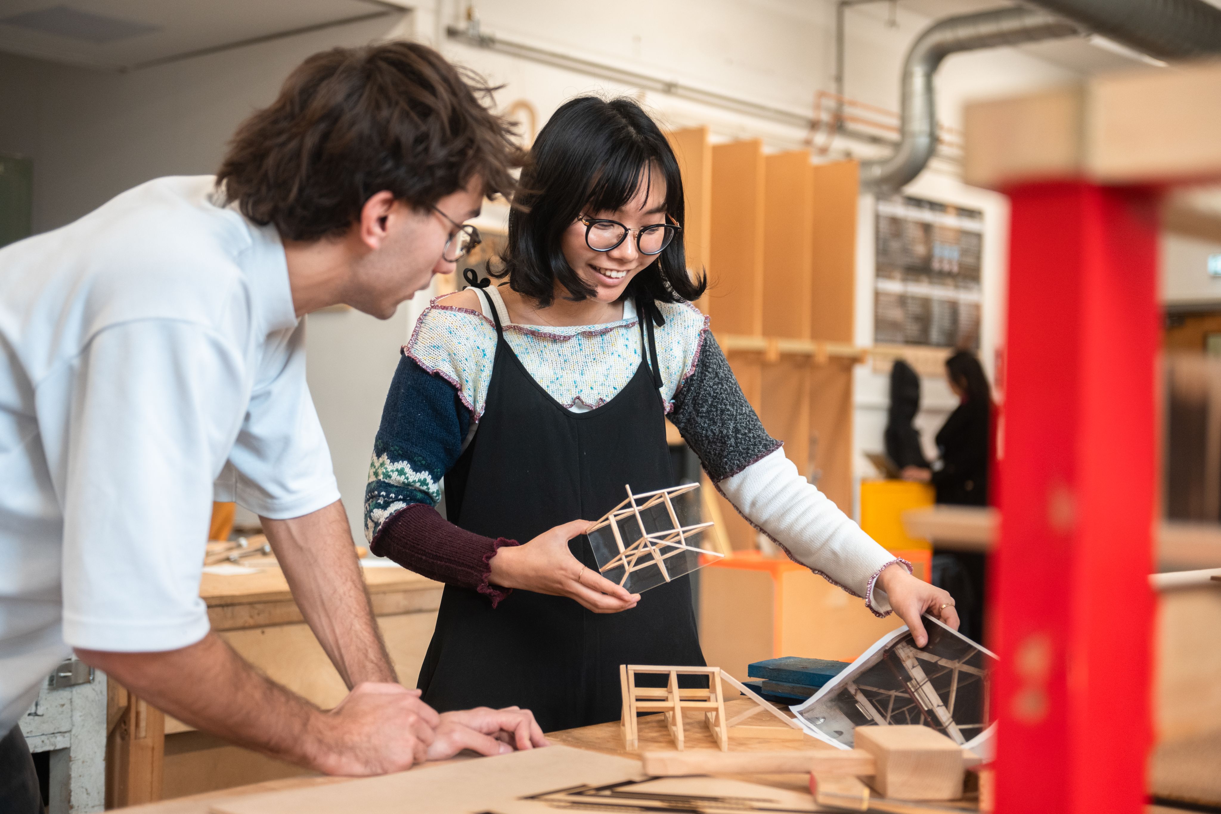 Two students stand in the architecture studios, holding wooden building models
