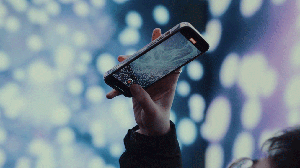 A hand holds a smart phone showing an augmented reality display against a projection of circular abstract patterns